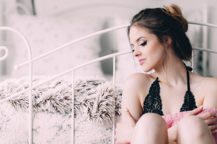 romantic boudoir photo of a girl sitting against a bed
