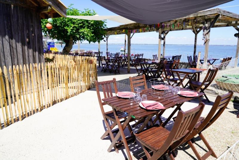 Beach terrace oyster restaurant in seaside with empty chairs and wood table on typical village of l`herbe in Cap Ferret France. A beach terrace oyster restaurant royalty free stock photography