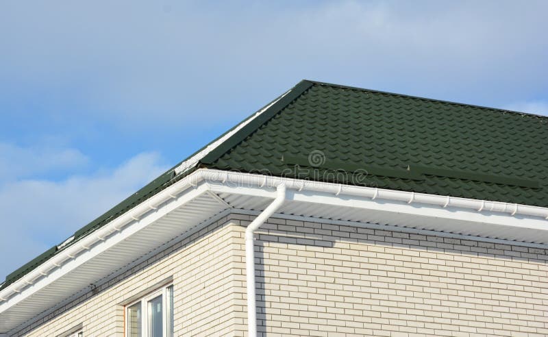 Brick house with green metal roof and rain gutter pipeline. Photo stock images