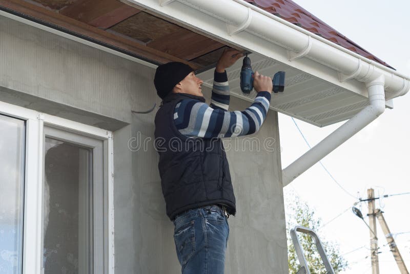 Installation of soffits. Construction worker mounts a soffit on the roof eaves stock photos