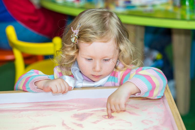 Cute child girl drawing draws developing sand in preschool at table in kindergarten stock images