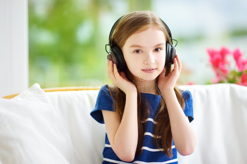 Cute girl wearing huge wireless headphones. Pretty child listening to the music. Schoolgirl having fun listening to kid`s songs at. Cute little girl wearing huge stock photos