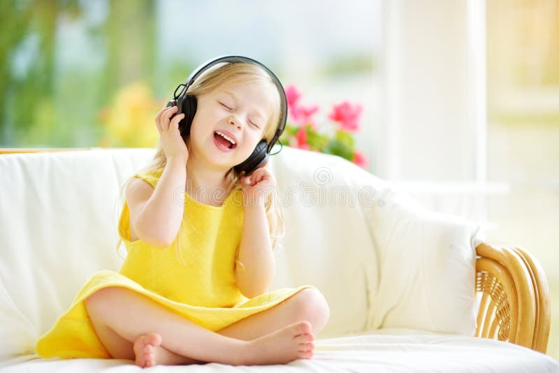 Cute girl wearing huge wireless headphones. Pretty child listening to the music. Schoolgirl having fun listening to kid`s songs at. Cute little girl wearing huge stock image