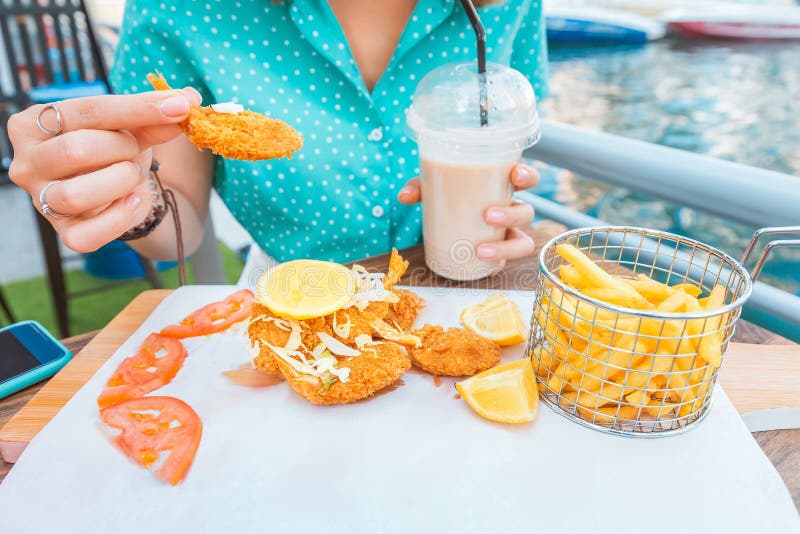 Girl eats prawns in batter and French fries on the terrace of a sea cafe. A girl eats prawns in batter and French fries on the terrace of a sea cafe stock photos