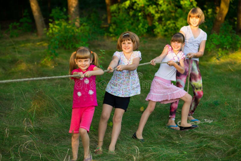 Group of happy children playing tug of war outside on grass. Kids pulling rope at park royalty free stock image