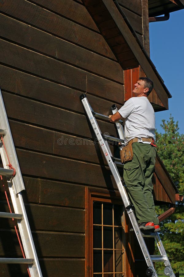 Handyman. A man on ladder prepares the side of a log home for a protective coat of stain stock photography