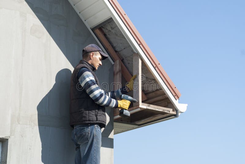 Installation of soffits. Construction worker mounts a soffit on the roof eaves stock photography