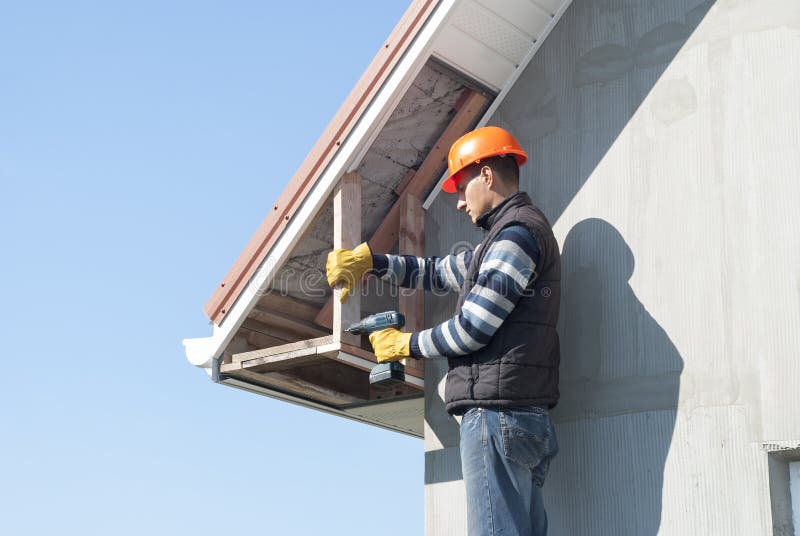 Installation of soffits. Construction worker mounts a soffit on the roof eaves stock images