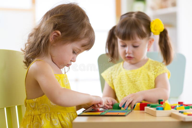 Kids playing with logical toy on desk in nursery room or kindergarten. Children arranging and sorting shapes, colors and stock photo