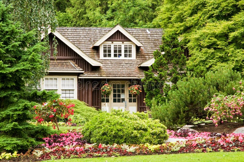 Landscaping log cabin. A view of a small log cottage secluded in the woods with colorful flower landscaping stock photo