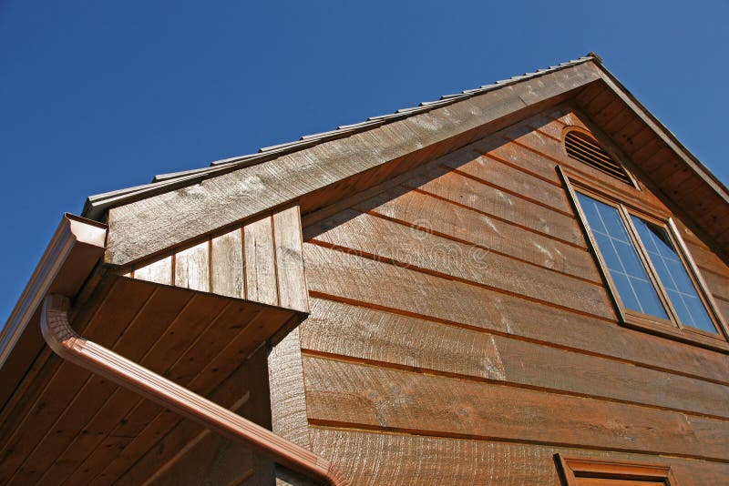 Log Siding. The gable end of a post and beam garage finished with log siding glows in the afternoon sun against a deep blue sky stock photo