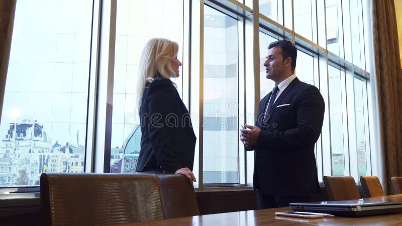 Business man and woman are standing by the panoramic window in their office. A men and a women are standing by the window in their office. The window is very royalty free stock photography