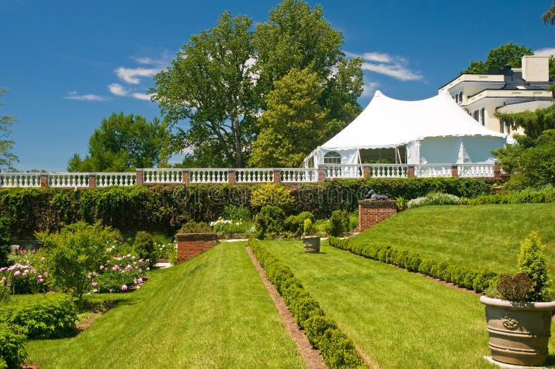 Party tent and garden. Large white party tent set up on a front lawn of a luxury mansion, overlooking an elaborate garden stock photography