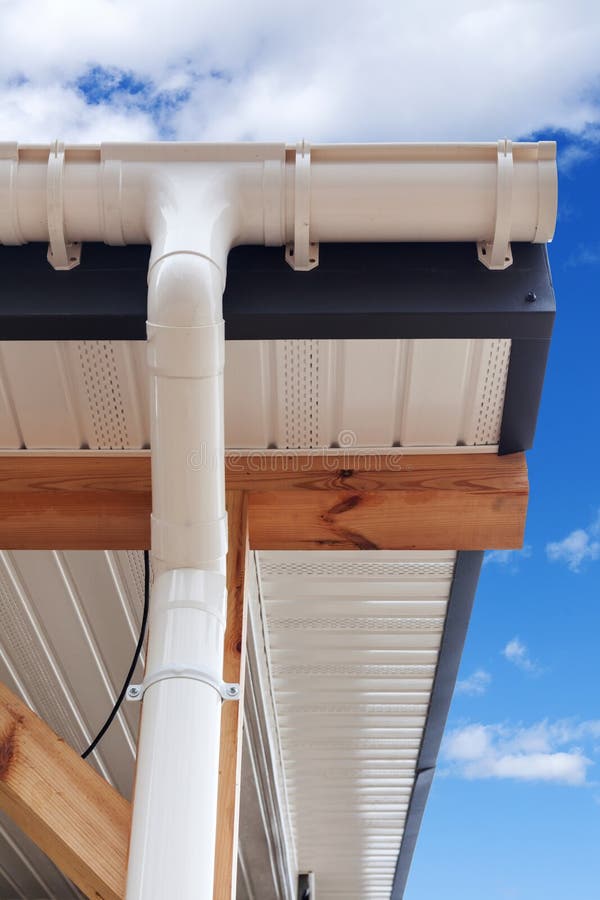 SIP panel house construction. New white rain gutter. Drainage System with Plastic Siding Soffits and Eaves against blue sky. SIP panel house construction. New royalty free stock photography