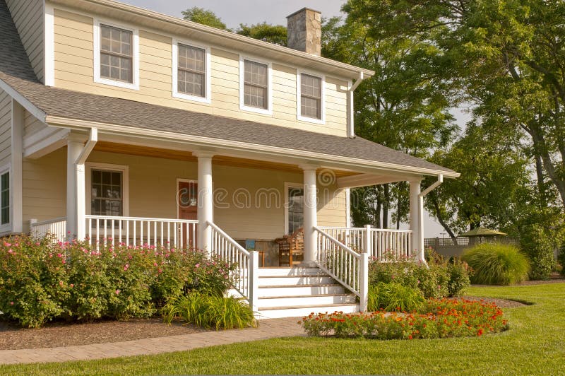 Suburban house with white porch. A view of a modest suburban house with a large white porch, colorful summer flowers and landscaping stock photography