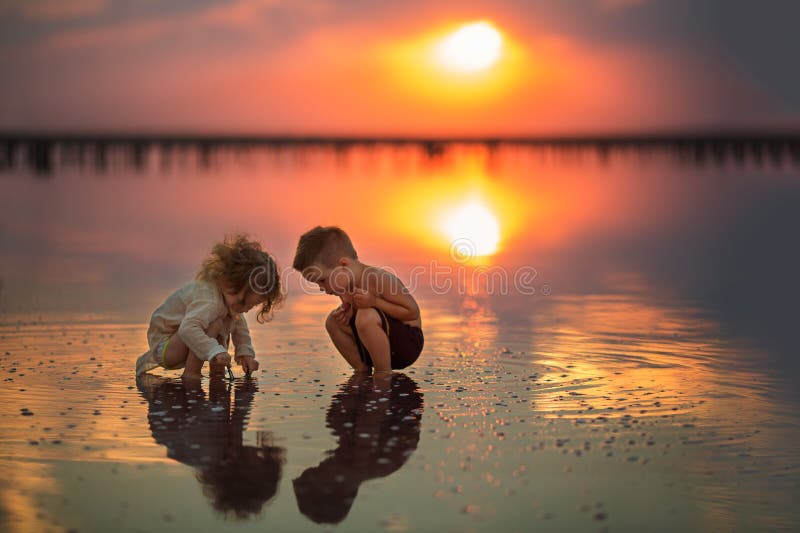 Two small children playing on the seashore during sunset royalty free stock image