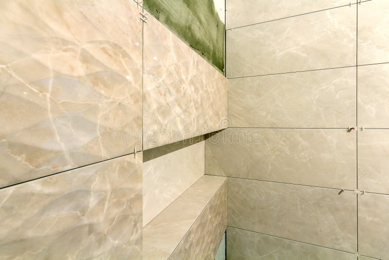 Unfinished work, light beige ceramic tiles installed on walls of bathroom or toilet. Tiles installation, home improvement,. Renovation and construction royalty free stock image