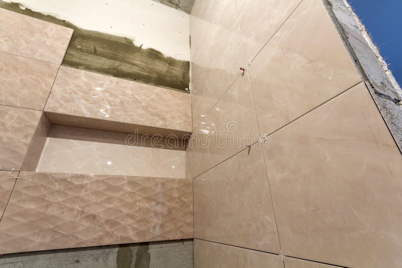 Unfinished work, light beige ceramic tiles installed on walls of bathroom or toilet. Tiles installation, home improvement,. Renovation and construction stock photography