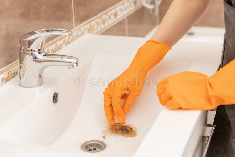 Woman cleaning company eliminates clogging of hair in sink, cleans tile.  stock photos