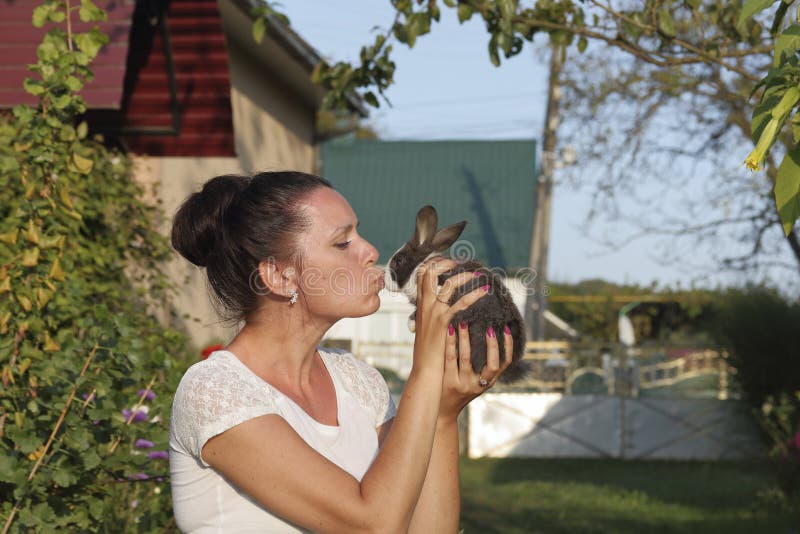 A woman holds a rabbit in her hands. Kisses him in the face. It stands in the courtyard of a private courtyard.  stock photo
