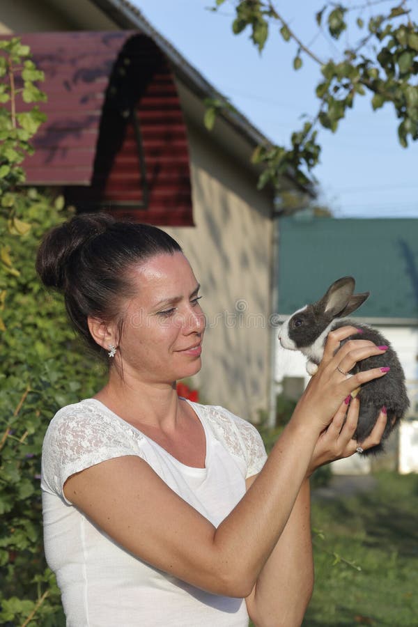A woman holds a rabbit in her hands. Presses it to the chest. It stands in the courtyard of a private courtyard.  stock image