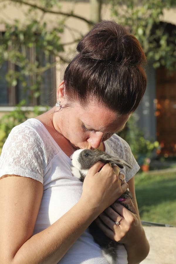A woman holds a rabbit in her hands. Presses it to the chest. It stands in the courtyard of a private courtyard.  royalty free stock photos