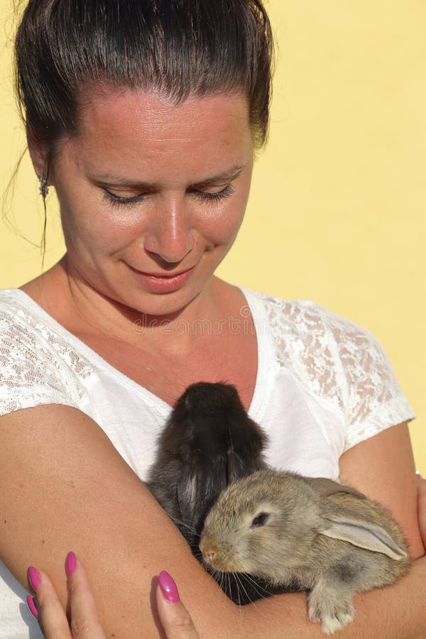 A woman holds a rabbits in her hands. Presses it to the chest. It stands in the courtyard of a private courtyard.  stock photo