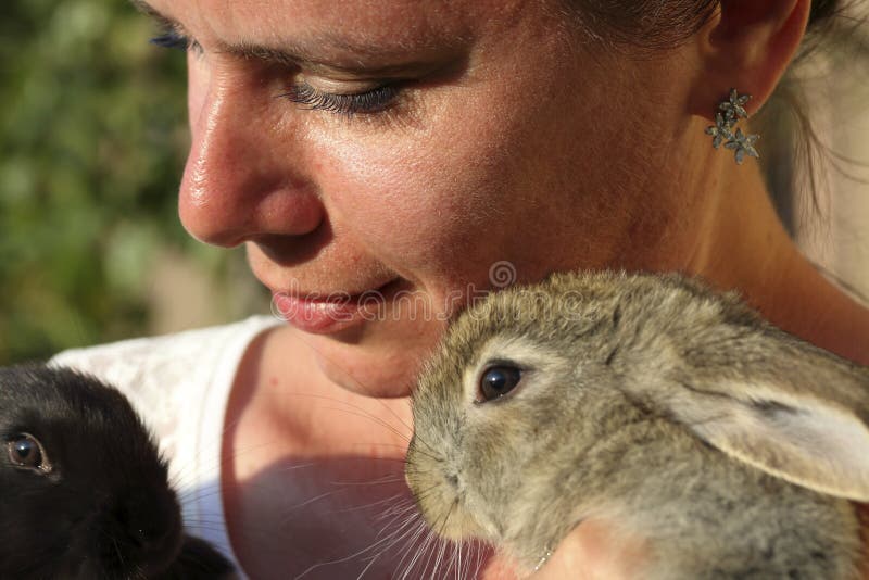 A woman holds a rabbits in her hands. Presses it to the chest. It stands in the courtyard of a private courtyard. Close-up.  stock image