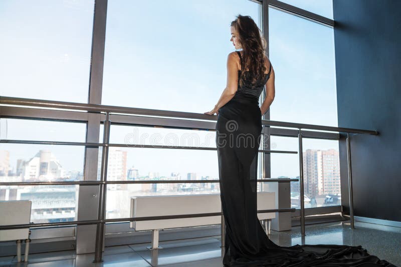 Young slender woman in a black dress opens the panoramic window in the room. Sad sad woman at big window. Young slender woman in a black dress opens the royalty free stock images